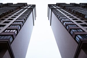 Two tall modern buildings photographed from ground level, creating a narrow bright gap between them.