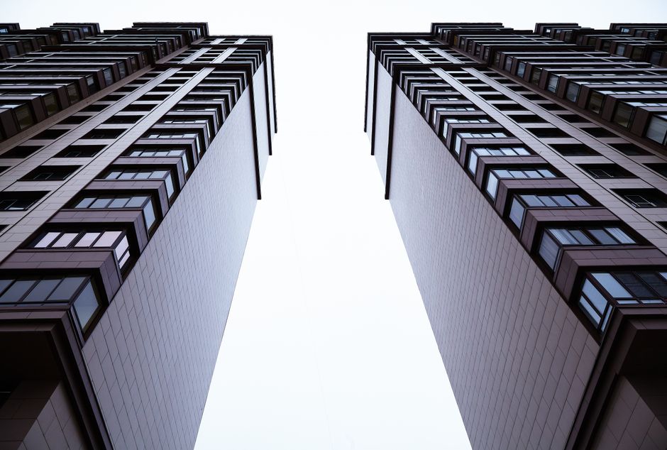 Two tall modern buildings photographed from ground level, creating a narrow bright gap between them.