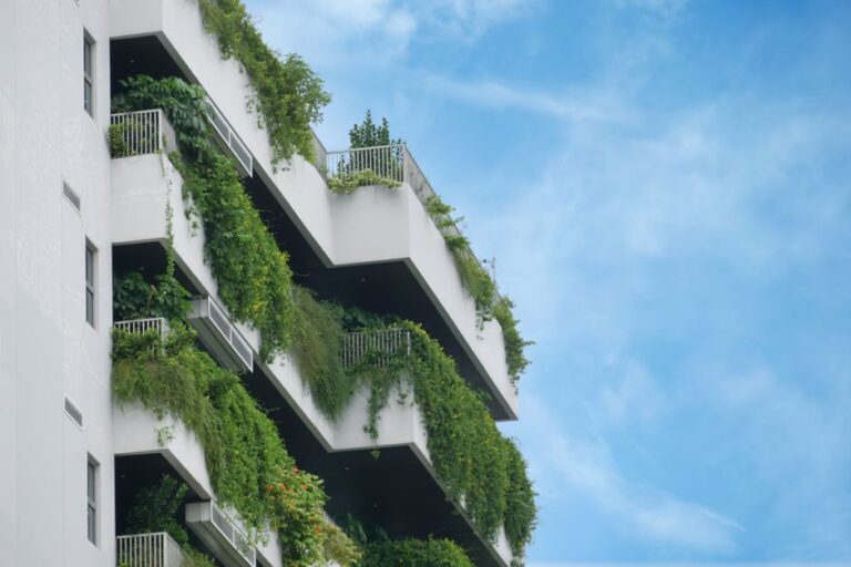 White multi-story building with balconies covered in cascading greenery against a blue sky, a vertical garden look.
