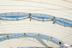 Interior view of a tensile-structure roof with curved blue skylight panels and metal supports.