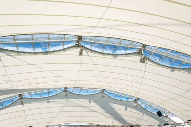 Interior view of a tensile-structure roof with curved blue skylight panels and metal supports.