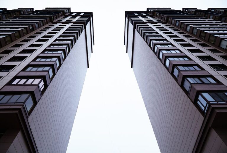 Two tall modern buildings photographed from ground level, creating a narrow bright gap between them.