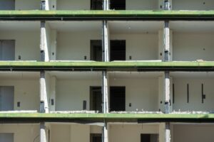 Multi-story unfinished concrete building under construction with green-painted balcony railings and open doorways on each floor.