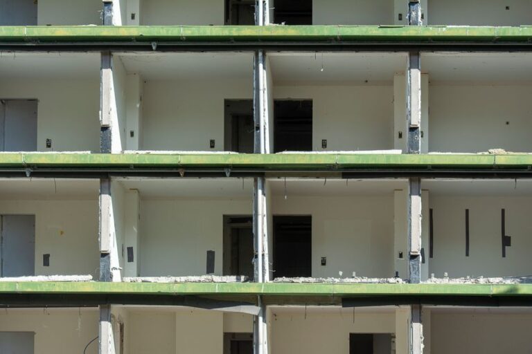 featured-14492911 - Awesim Building Consultants Multi-story unfinished concrete building under construction with green-painted balcony railings and open doorways on each floor.