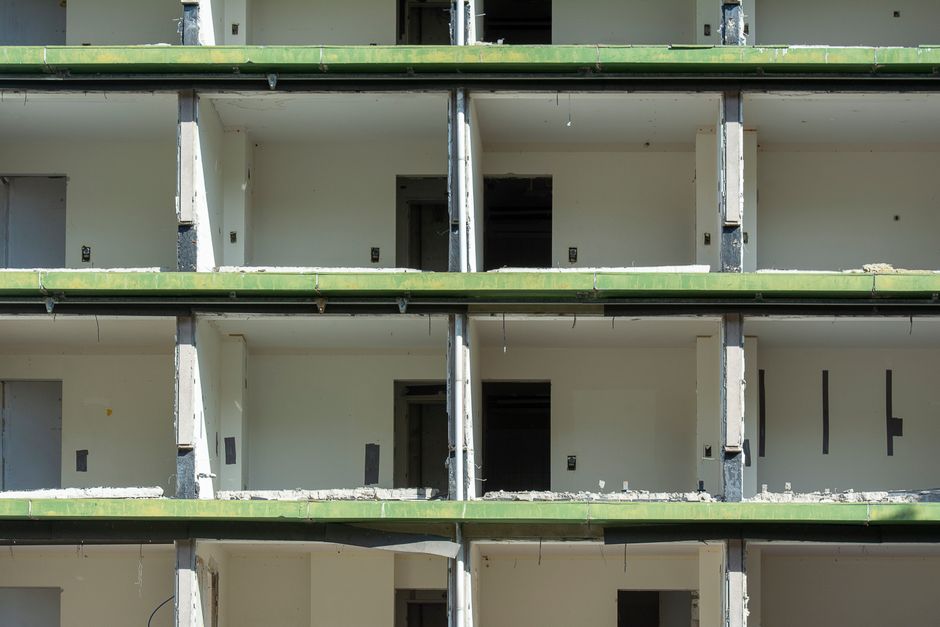 featured-14492911 - - Multi-story unfinished concrete building under construction with green-painted balcony railings and open doorways on each floor.