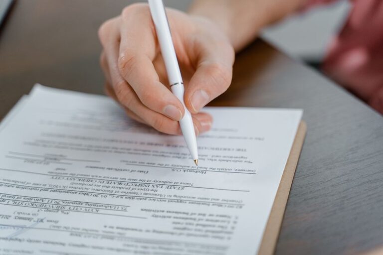 Person filling out a form on a clipboard with a white pen held in a right hand.