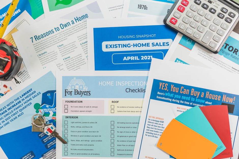 A collage of real estate flyers and documents, including a blue 'Existing-Home Sales' card, inspection checklists, and a calculator with a colorful spread of pamphlets.