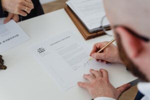 Person signs a divorce decree document at a desk, with another document nearby and a pen in hand.