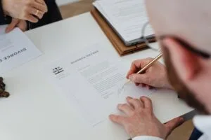 featured-7876037 - Awesim Building Consultants Person signs a divorce decree document at a desk, with another document nearby and a pen in hand.