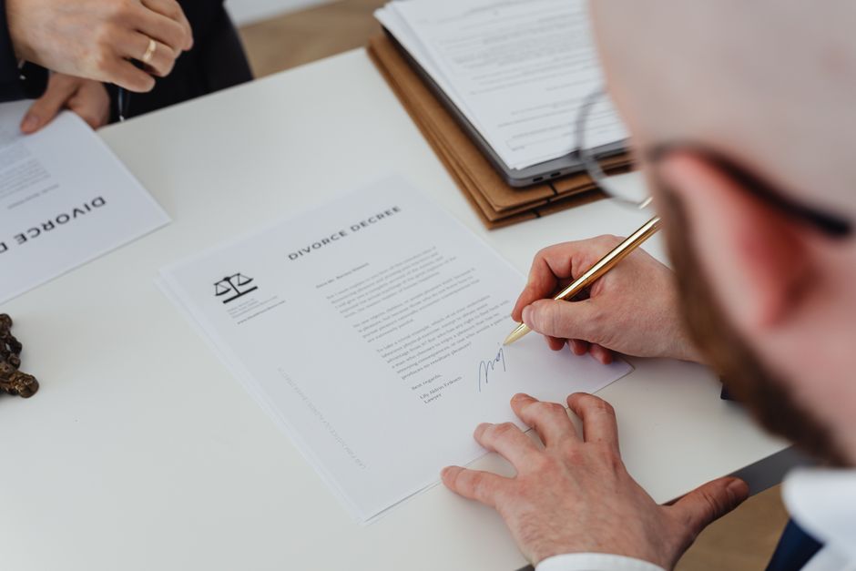 Person signs a divorce decree document at a desk, with another document nearby and a pen in hand.